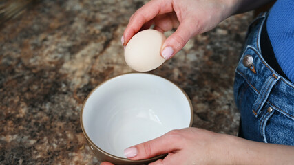 Close up of a woman holds an egg and is about to break it, cooking a dish concept.