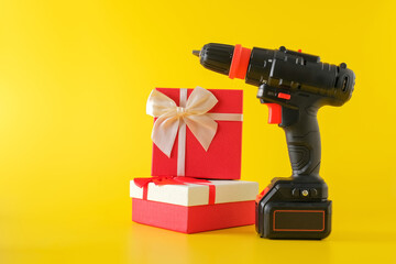 Handheld cordless power drill, hand battery screwdriver and gift boxes on yellow background....