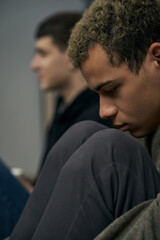 Staged photo illustrates problems and conflicts in gay couple relationships. Moment of showdown: two young men are sitting on the floor near each other. Partners are upset and wistful.