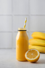 Yellow smoothie in a bottle with a straw, lemon and bananas. The concept of healthy eating. Copy space.