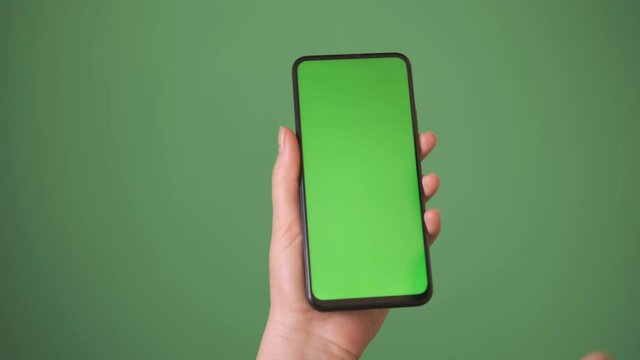 Phone in the hand close up isolated at green background. Phone screen is green chroma key, background chroma key green screen
