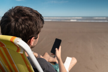 Young man on vacation at the beach using his smart phone.