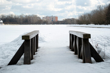 Panoramic views of the frozen lake, forest and houses. Wooden bridge over the stream