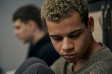 Staged photo illustrates problems and conflicts in gay couple relationships. Moment of showdown: two young men are sitting on the floor near each other. Partners are upset and wistful.