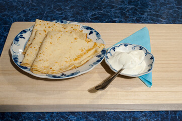 Two pancakes on a white plate. Sour cream on a small saucer. Maslenitsa.