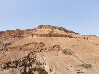 Fototapeta premium A sandy mountain that used to be bottom of Dead Sea stands near Ein Bokek embankment on the coast of the Dead Sea, the sea itself and the mountains of Jordan visible in the distance, in Israel