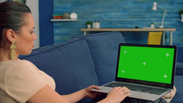 Business woman working on communication project for company uses isolated laptop computer with mock up green screen chroma key lying on sofa in living room. Freelancer using technology concept