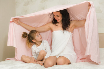 Mother and her daughter playing and hugging in the bed. Happy loving family. Happy mother's day.