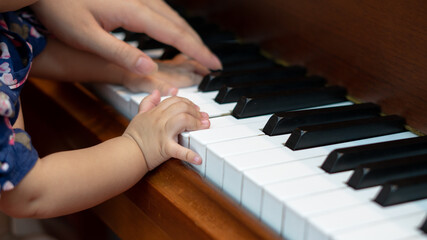 Fototapeta premium Side view of Baby Girl's Hands playing with Piano Keys with an adult