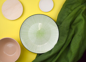 Mock up composition with empty ceramic tableware, green fabric on yellow background. Minimalist summer kitchen setting. Eco friendly style. Trendy color design. Top view. Flat lay.