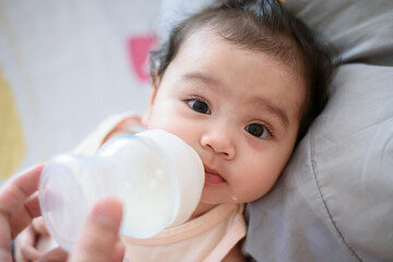 Cute little asian baby girl I was drinking from the bottle fed by my mother looking at the camera