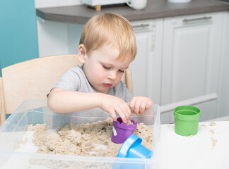 Baby boy playing with kinetic sand at home. Early age education. Toddler playing