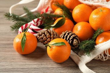 Fresh tangerines, Christmas candy canes, fir tree branches and cones in mesh bag on wooden table,...