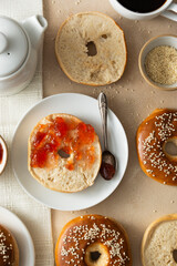 Bagels pastry buns for breakfast,with coffee cup and fruit jam. Top view, bright background, natural light.