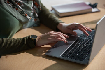 Close-up of woman sitting at the table and typing on laptop computer during her work at office