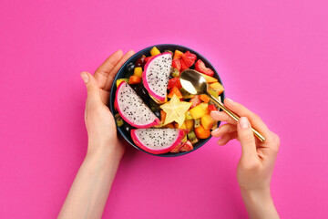 Woman with bowl of delicious exotic fruit salad on pink background, top view