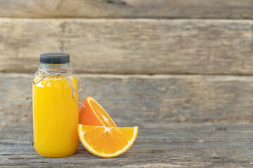 A bottle of orange juice and sliced orange on a wooden background