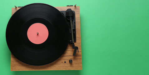 Modern turntable with vinyl record on green background, top view