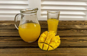 Still life with mango and glass jug with juice on an old wooden background