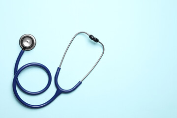 Stethoscope on light blue background, top view. Space for text