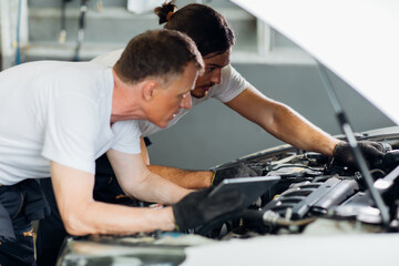 Two caucasian male mechanic repairs car in garage. Car maintenance and auto service garage concept. Closeup hand and spanner. teamwork concept.