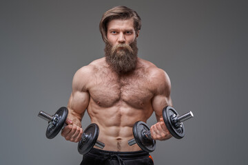 Fototapeta na wymiar Masculine guy with sportive body holding dumbells in gray background