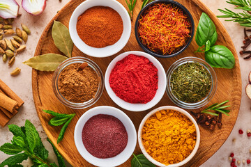 Fototapeta na wymiar Colorful herbs and spices for cooking: turmeric, dill, paprika, cinnamon, saffron, basil and rosemary. Indian spices in wooden plate. On light brown stone background. Top view.