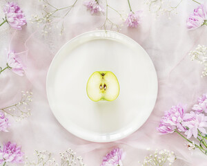 Obraz na płótnie Canvas The concept of spring cleansing, detox, diet and weight loss. Romantic, spring, floral composition for beauty blogging with half a green apple on a white plate. Horizontal banner, top view