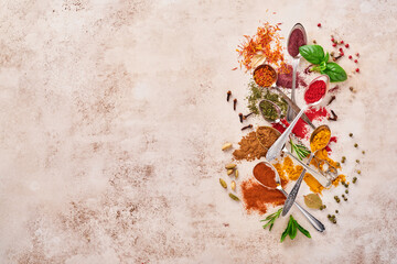 Colorful herbs and spices for cooking: turmeric, dill, paprika, cinnamon, saffron, basil and rosemary in a spoon. Indian spices. On light brown stone background. Top view.
