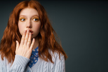 Young ginger shocked woman looking aside and covering her mouth