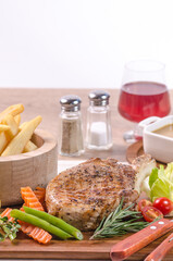 The delicious grilled ribeye beef steak on the wooden cutting board with french fries and fresh vegetables salad.