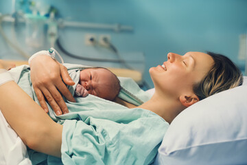 Mother and newborn. Child birth in maternity hospital. Young mom hugging her newborn baby after delivery. Woman giving birth. - 421048627