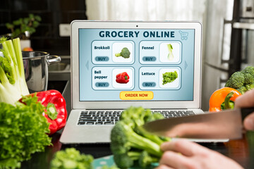 Man using laptop and cooking in kitchen at home. Grocery shopping online. Web page of online food store on the screen Fresh vegetables on kitchen counter. Healthy lifestyle and social media concept.
