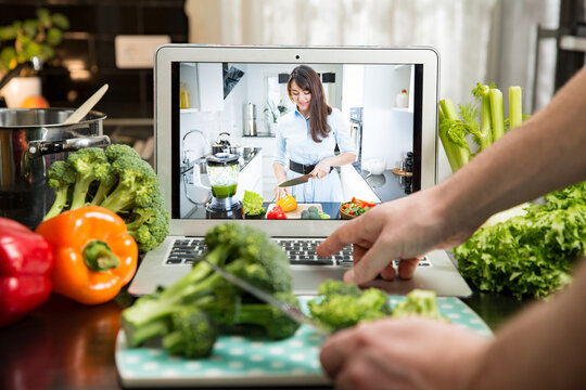 Beautiful happy woman streaming broadcast video blog about tasty and healthy food from home kitchen. Healthy lifestyle and social media. Man watching video recipe on laptop and cooking at home.