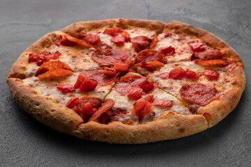 whole fresh round pizza with pepperoni and mozzarella cheese on a gray table. tasty fast food background in pizzeria close-up