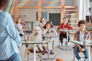 Happy mixed kid pupils in elementary school lesson with a dog in center