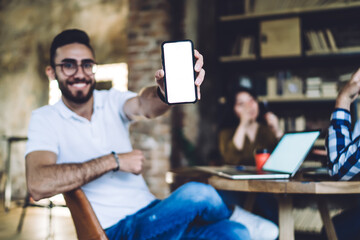 Positive man demonstrating smartphone screen while cooperating with colleagues