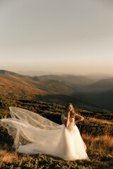 Fototapeta na wymiar Beautiful bride in a white wedding dress stands posing in the sun and smiles in the mountains