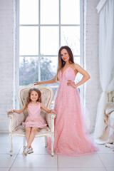 Mom and daughter in luxurious, pink, lush dresses. Family clothes, identical dresses. The background is beautiful, expensive, white, classic interior. Artistic, family photography