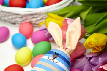 Easter bunny doll and Easter eggs in basket and spring colorful flowers on white wooden table