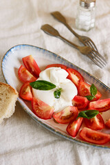 Traditional Italian salad with Burrata cheese, tomatoes and fresh basil. Mozzarella burrata salad with basil leaves and tomatoes on plate on beige linen tablecloth