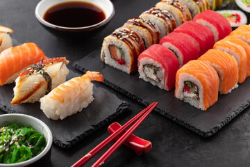 Sushi rolls set, nigiri sushi and soy sauce on a black textured background and chopsticks on the side. Traditional Japanese food, angle view.
