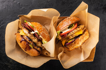 Two large grilled chicken burgers in a craft box on a dark background, top view. Takeaway hamburger. Burger in the box, fast food. - obrazy, fototapety, plakaty
