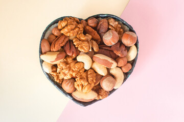 Organic mixed nuts in a heart-shaped bowl. Assorted nuts: hazelnuts, walnuts, Brazilian nuts, pecans, pistachio, almonds, cashews. Healthy food for the heart, useful microelements and vitamins.
