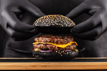 Close-up, finishing touch making grilled burger. Chef hands in black gloves are closing top black...