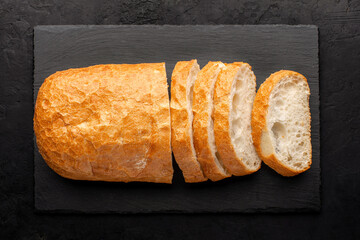 Top view of sliced ciabatta on a slate board, black rustic background.