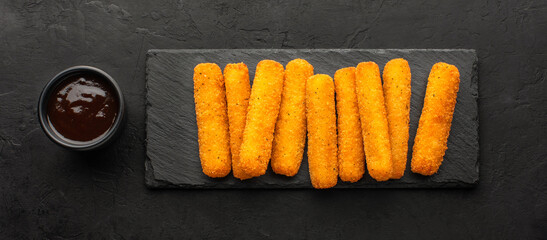 Cheese sticks set and bowl with sauce on the side on a slate board, top view, black rustic...