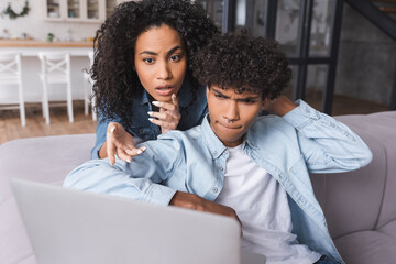 Pensive african american couple looking at laptop on blurred foreground