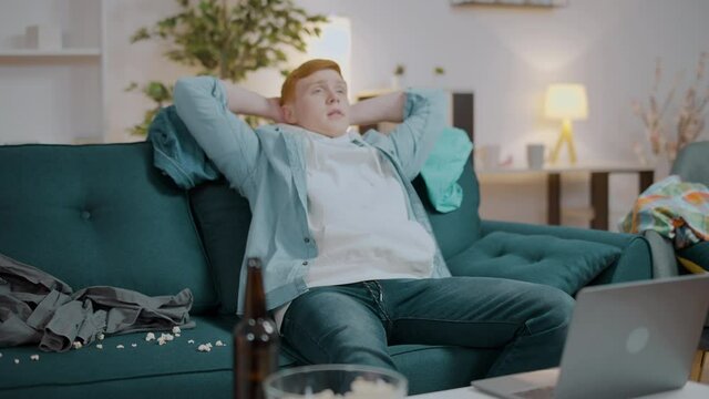 Young lazy man in dirty clothes sitting on couch, procrastination and boredom