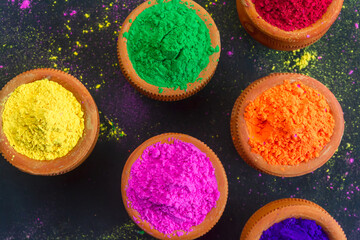 Eco-friendly colorful holi powder or gulal in earthen pot on black background.